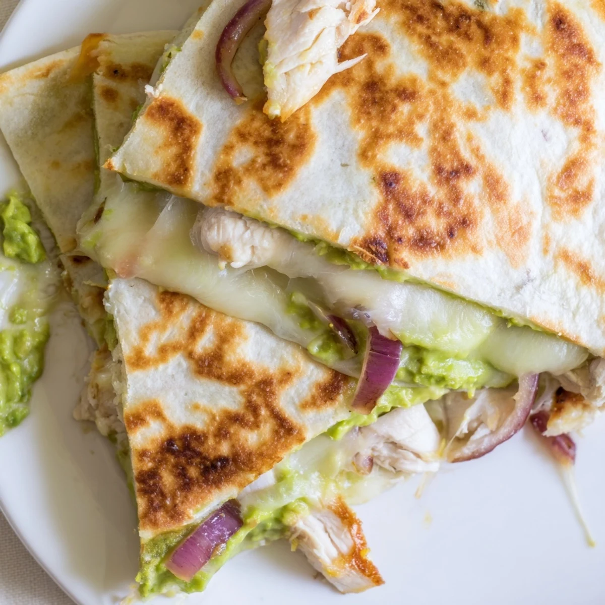 Golden-brown Chicken Avocado Quesadilla wedges reveal melted cheese and creamy avocado filling on a rustic plate.  