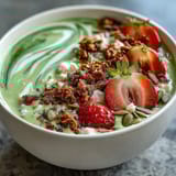 Vibrant strawberry matcha latte smoothie bowl topped with fresh strawberries, crunchy granola, and chia seeds.  