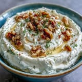 Velvety feta and cream cheese blend, drizzled with honey and olive oil, sprinkled with walnuts and herbs for a Mediterranean appetizer.  