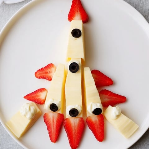 Image of a creative Retro Rocket snack platter; cheddar cheese body with vibrant strawberry flames.