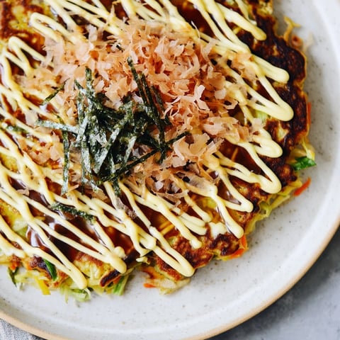 Golden-brown Japanese Okonomiyaki Pancakes sizzling on a griddle, topped with creamy mayo, tangy sauce, and dancing bonito flakes.