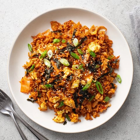 A close-up of vibrant Spicy Kimchi Fried Rice sizzling in a cast-iron skillet, with steam rising from the bright red, caramelized kimchi and fluffy rice.  