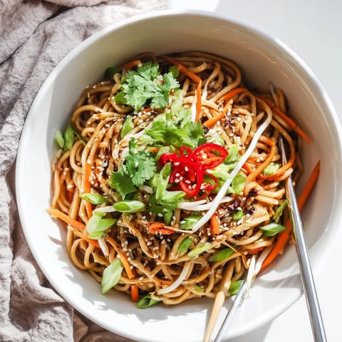 A close-up of a savory Asian Garlic Noodle Bowl with glossy noodles coated in a garlic-butter sauce, topped with green onions and sesame seeds.  