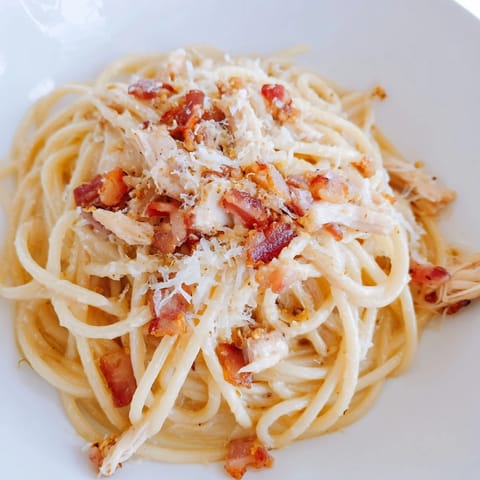 Steaming plate of homemade Chicken Carbonara with tender pasta, savory shredded chicken, and crispy bacon, garnished with fresh parsley and extra Parmesan for a classic Italian-American dinner.  