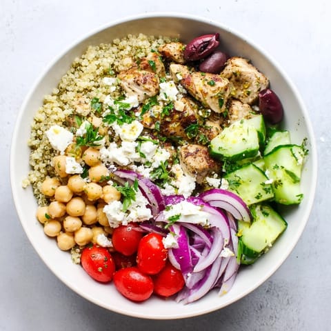A close-up of a Mediterranean Chicken Bowl featuring tangy olives, cherry tomatoes, and a drizzle of zesty lemon-oregano dressing.