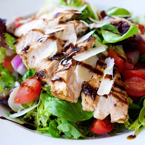 Juicy bruschetta chicken salad arranged on a white platter, featuring diced tomatoes, red onion, and fresh basil over mixed greens.  