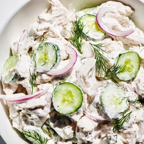 Bright green cucumber slices and shredded chicken tossed in creamy dill yogurt dressing, served chilled in a white bowl.  