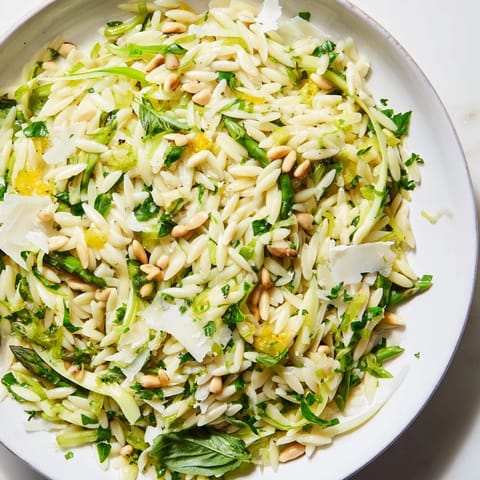 A vibrant bowl of Asparagus Lemon Orzo Salad featuring shaved asparagus ribbons, Parmesan, and toasted pine nuts on a wooden table.