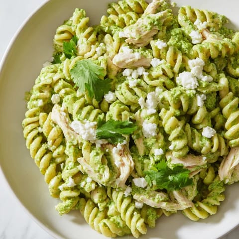 A close-up of creamy cilantro lime chicken pasta in a white bowl, with lime wedges and a sprinkle of cotija cheese for a fresh, zesty finish.