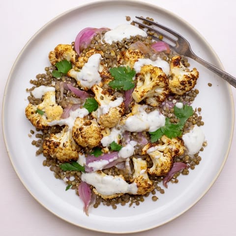 A vibrant serving of Roasted Cauliflower With Lemon Lentil Cumin Tahini Yogurt, featuring caramelized cauliflower and a rich, garlicky sauce.  