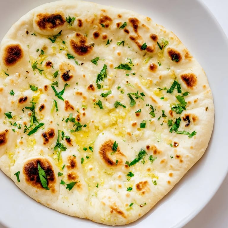 Freshly cooked garlic naan with pillowy textures and browned spots, perfect for dipping into savory dishes.