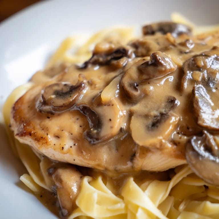 A close-up of tender Chicken Marsala with a rich, velvety mushroom sauce spooned over al dente pasta, garnished with fresh parsley.  