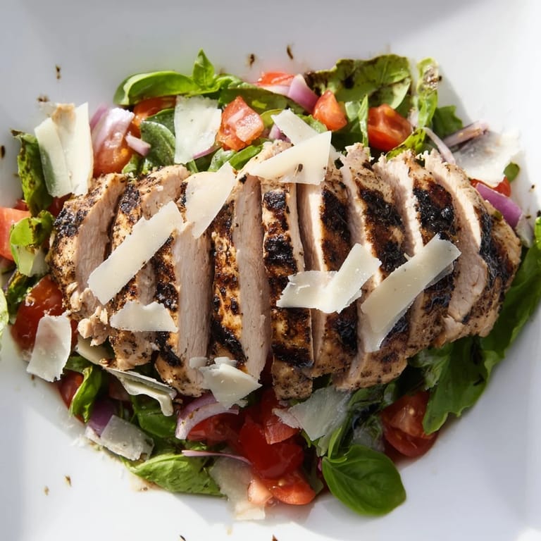 A hearty bowl of bruschetta chicken salad with zesty tomato-basil topping, glistening olive oil, and optional shaved Parmesan on top.