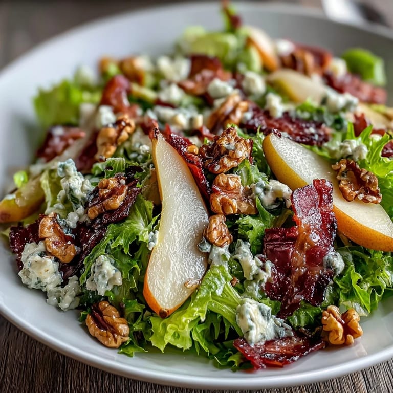 Fresh pear slices and blue cheese crumbles atop frisée greens, with crispy prosciutto and walnuts in a salad bowl.